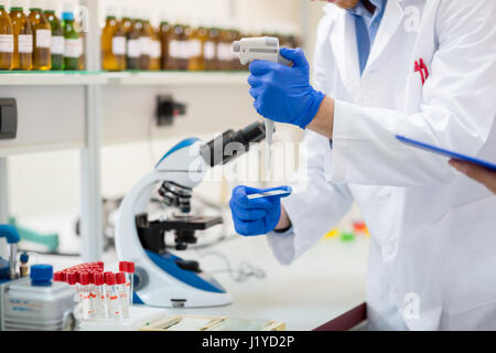 Scienziato chimico luogo campione di liquido con pipetta di campionamento sul vetrino del microscopio Foto Stock