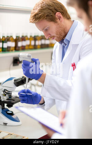 Nel laboratorio chimico maschio scienziato luogo campione di liquido sul vetrino del microscopio Foto Stock