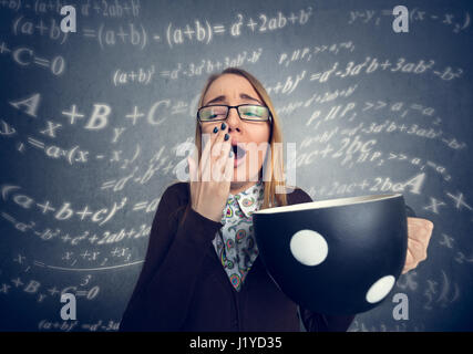 Stanco schoolgirl sbadigli con grande tazza di caffè Foto Stock