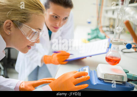 Due assistenti donne regolare dispositivo per misurare liquido nel laboratorio chimico Foto Stock