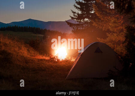 Tenda per gli escursionisti in montagna in serata con un falò con scintille vicino ad essa Foto Stock