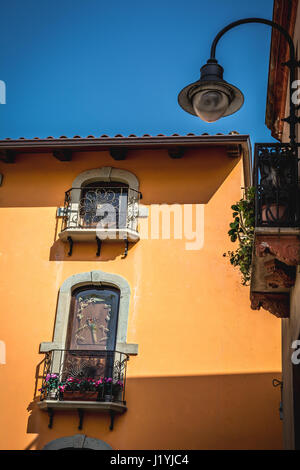 Finestre di un edificio arancione con splendidi balconi e fiori e lanterna in Arbus, Sardegna, Italia. Foto Stock