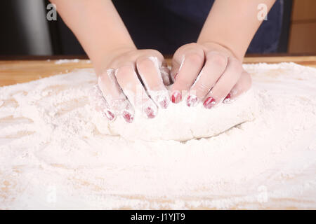 Close-up di donna mani impastare la pasta su un tavolo di legno. Cucina e panificazione concetto. Foto Stock