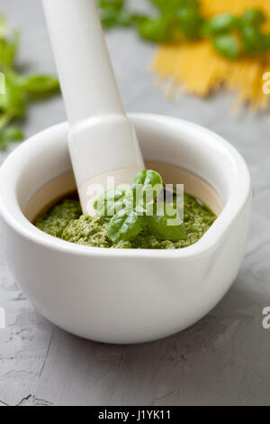 Pesto di basilico in un mortaio bianco su un cemento grigio sfondo Foto Stock