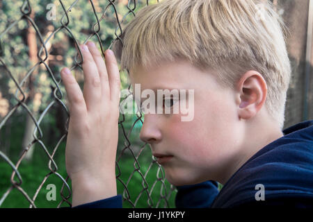 Triste, arrabbiato, frustrato boy (bambino, capretto, teen) vicino a maglia metallica, close up ritratto, bambini adolescente problemi concetto. Foto Stock