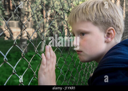 Triste, arrabbiato, frustrato boy (bambino, capretto, teen) vicino a maglia metallica, close up ritratto, bambini adolescente problemi concetto. Foto Stock