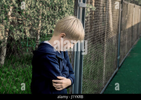 Triste, arrabbiato, frustrato boy (bambino, capretto, teen) vicino a maglia metallica, close up ritratto, bambini adolescente problemi concetto. Foto Stock