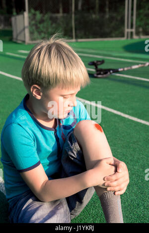 Ragazzo con un ginocchio raschiata all'aperto. Avvolto sul ginocchio del ragazzo dopo l'incidente. Foto Stock