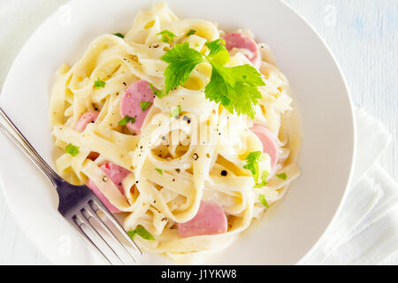 Alfredo tagliatelle con salsicce e verdi su piastra bianca - fatti in casa pasta cremosa Foto Stock