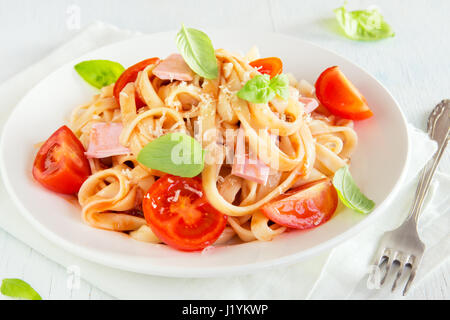 Tagliatelle al prosciutto, salsa di pomodoro, pomodori ciliegini e le foglie di basilico sulla piastra bianca - deliziosi piatti fatti in casa tagliatelle Foto Stock