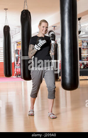 Giovane donna tatuata, boxe a sandsack in un boxing studio, Baviera, Germania Foto Stock