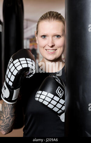 Giovane donna tatuata, boxe a sandsack in un boxing studio, Baviera, Germania Foto Stock