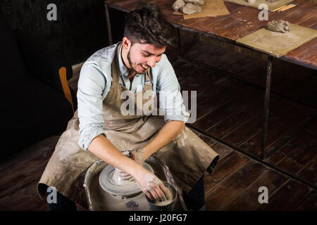 Creazione di mug da argilla su un twisted tornio del vasaio. Lo scultore in officina rende una brocca di terracotta. Foto Stock