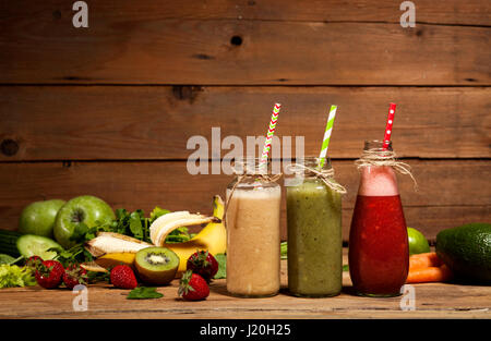 Assortimento di frutta e verdura frullati in bottiglie di vetro con cannucce su sfondo di legno. Foto Stock