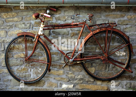 Vecchio arrugginito bicicletta appesa sul muro di pietra. Foto Stock