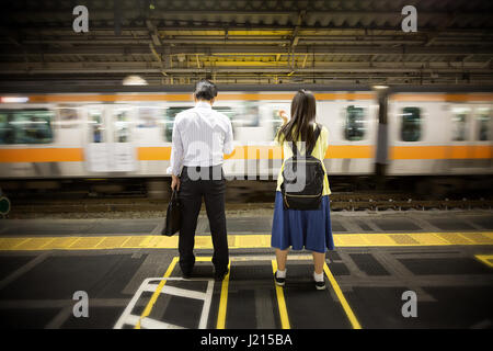 Imprenditore non identificato e schoolgirl attendere per il quotidiano treno dei pendolari. Tokyo, Giappone. Foto Stock