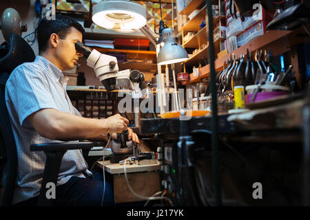 Gioielliere lavorando su metalli con dispositivo ottico che consente per lavori di precisione Foto Stock