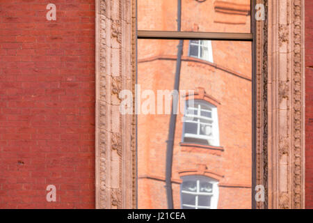 La riflessione di un vecchio edificio in mattoni a Londra in un una finestra con elaborati stampaggio, Londra Inghilterra, Regno Unito Foto Stock