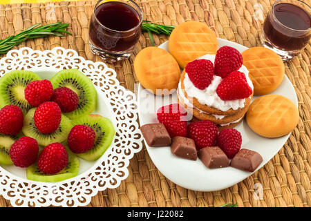 Fresche Lamponi rosso su bianco artistica targa / rosso dei lamponi freschi su un bianco artistica targa con i cookie, rosmarino, cioccolato e crema di panna in b Foto Stock