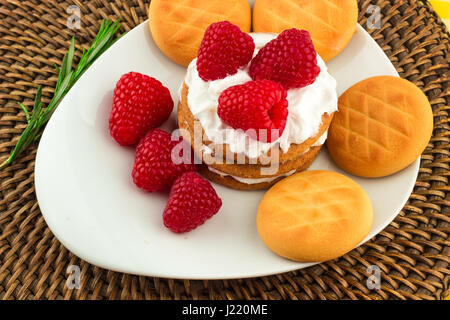 Fresche Lamponi rosso su bianco artistica targa / rosso dei lamponi freschi su un bianco artistica targa con i cookie, rosmarino, cioccolato e crema di panna in b Foto Stock