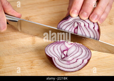 Vista sulle mani di un uomo di trinciatura fresche Sbucciate la cipolla rossa per pranzo un bambù tagliere. Foto Stock