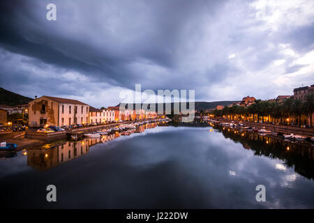 La città di notte vista del porto di Bosa, Sardegna, Italia. Case colorate e blu cielo drammatica che riflette nell'acqua. Foto Stock