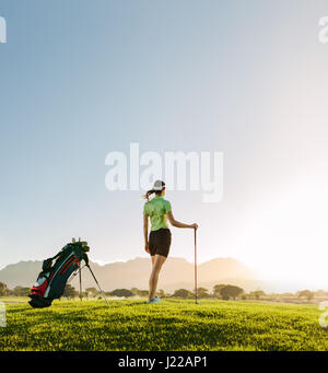 Per tutta la lunghezza della giovane donna in piedi sul campo da golf su un giorno d'estate. Vista posteriore del giocatore di golf femminile con golf club sul campo guardando lontano. Foto Stock