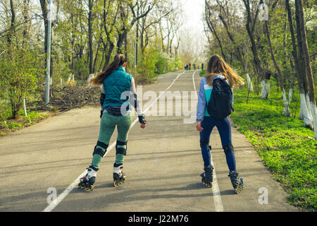 Due ragazze su pattini a rotelle corrono lungo la strada accanto a ciascun altro Foto Stock