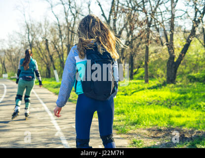 Due ragazze su pattini a rotelle corrono lungo la strada accanto a ciascun altro Foto Stock