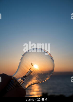 Uomo con lampadina della luce al tramonto, verde concetto energetico Foto Stock