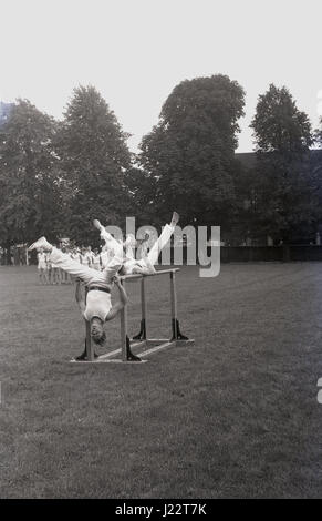 1950, storico, due maschio ginnasti sulle barre parallele la visualizzazione di ginnastica artistica di competenze al di fuori di un campo. Foto Stock