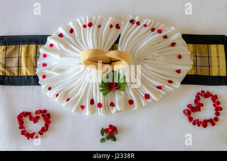 Asciugamano come uccelli con decor di rosso petali di rosa su bianco letto pulito nella camera di albergo, aspetto di cui sopra. Foto Stock