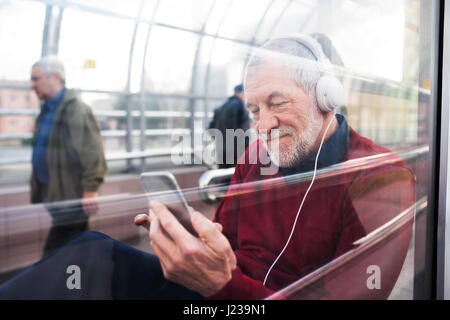 L'uomo anziano con lo smartphone e le cuffie sono seduti in passaggio. Foto Stock