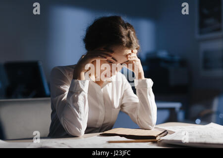 Stanco di sesso femminile guardando il disegno nel blocco note mentre si lavora nella notte Foto Stock
