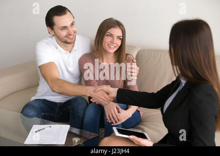 Felice coppia giovane e broker di handshaking manager dopo la firma Foto Stock