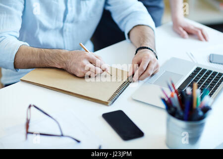 Closeup colpo di mani maschio iscritto negli appunti mentre si lavora alla scrivania in ufficio Foto Stock