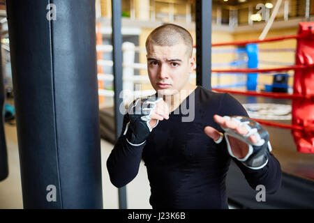 Ritratto di determinata giovane uomo muscolare in piedi nella lotta pongono e guardando la telecamera durante la pratica di inscatolamento nel club sportivo Foto Stock