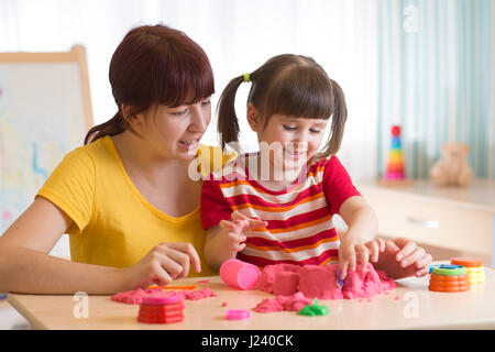 Un incantevole piccola bambina e la sua mamma gioca con la sabbia cinetica a casa Foto Stock