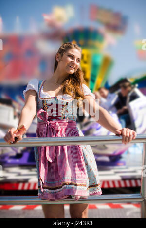 Attraente giovane donna alla luna park tedesco Oktoberfest con tradizionale dirndl e joyride in background Foto Stock