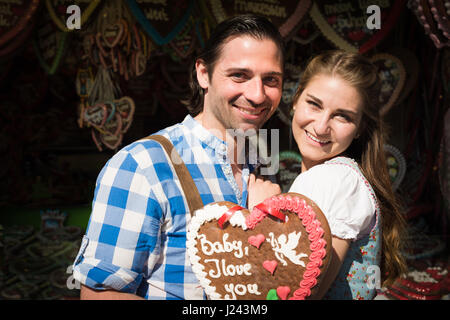 Coppia giovane in amore in tradizionale costume tedesco (dirndl e pantaloni in pelle) l'Oktoberfest, egli sta dando il suo un panpepato cuore Foto Stock