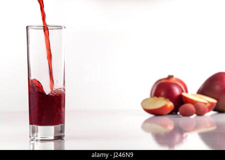Il flusso di succo rosso versando in un bicchiere. Composizione di frutta. Foto Stock