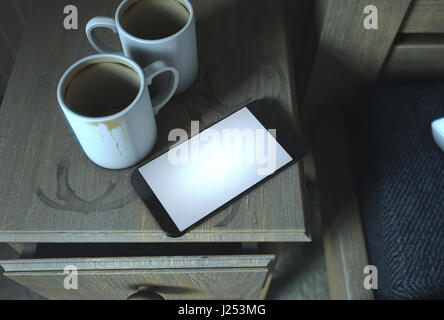 Un vero e proprio concetto life scena mostrando un comodino con sporco tazze da caffè e un generico smartphone illuminata di notte - 3D Render Foto Stock