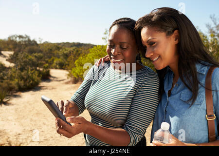 Madre e figlia adulta navigare con il cellulare a piedi Foto Stock