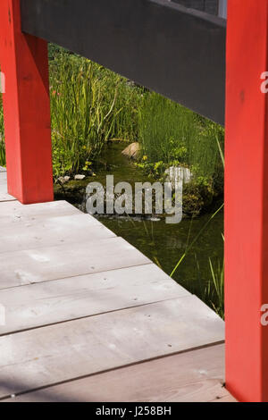 Vista di una piccola cascata in un laghetto ornamentale attraverso una passerella di legno in un residenziale paesaggistico cortile anteriore giardino in estate Foto Stock