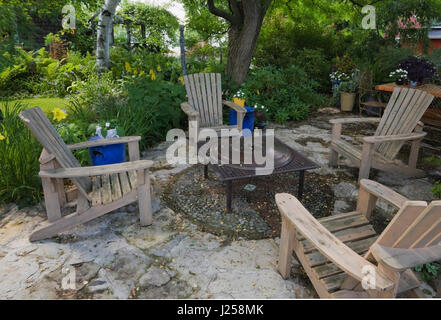 Legno sedie adirondack intorno a un tavolo sul patio in lastricato in un cortile paesaggistico giardino in estate Foto Stock