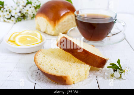 Una tazza di tè con un morbido bun, le fette di limone è un buon modo per iniziare la giornata. La prima colazione. Foto Stock