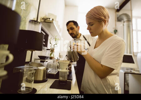 Barista femmina versando acqua calda attraverso imbuto in coffee shop Foto Stock