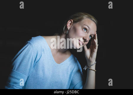 Considerato giovane donna che guarda verso l'alto contro lo sfondo nero Foto Stock