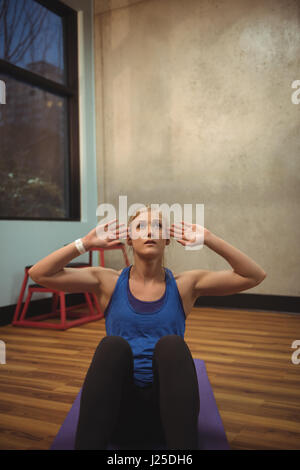 Montare donna eseguendo sgranocchia su un tappetino di ginnastica in palestra Foto Stock