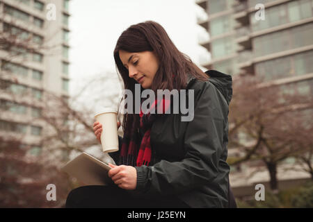 Donna felice azienda tablet e la tazza di caffè seduti in città Foto Stock